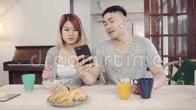 漂亮的亚洲年轻夫妇在吃早餐时，一边拿着报纸和手机，一边在桌子上<strong>分心</strong>。